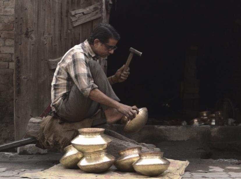 Craftsman hammering metal at a workshop bench